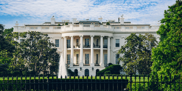 The White House on a sunny day with a fountain in front and a black fence in the foreground.